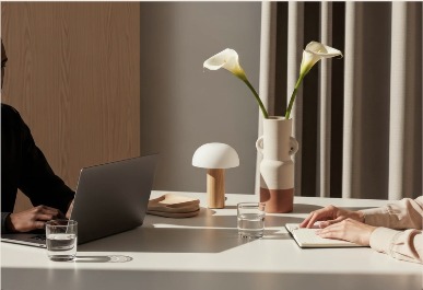 Sunlit desk with calla lilies in a ceramic vase, a small lamp and a laptop